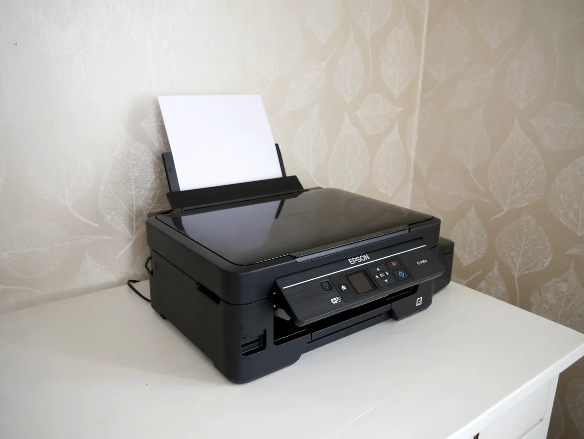 Fotografia real de uma Epson EcoTank ET-2550 com papel carregado sobre uma mesa clara